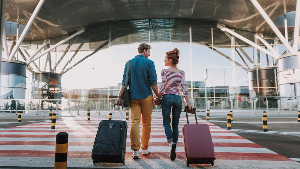 A couple walking with suitcases holding hands